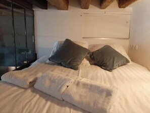 A bed with a white cover and two pillows, a wooden ceiling, and a white wall. - Beautiful, Air-Conditioned Apartment in Aix, Right in the Heart of Downtown (ile de france)