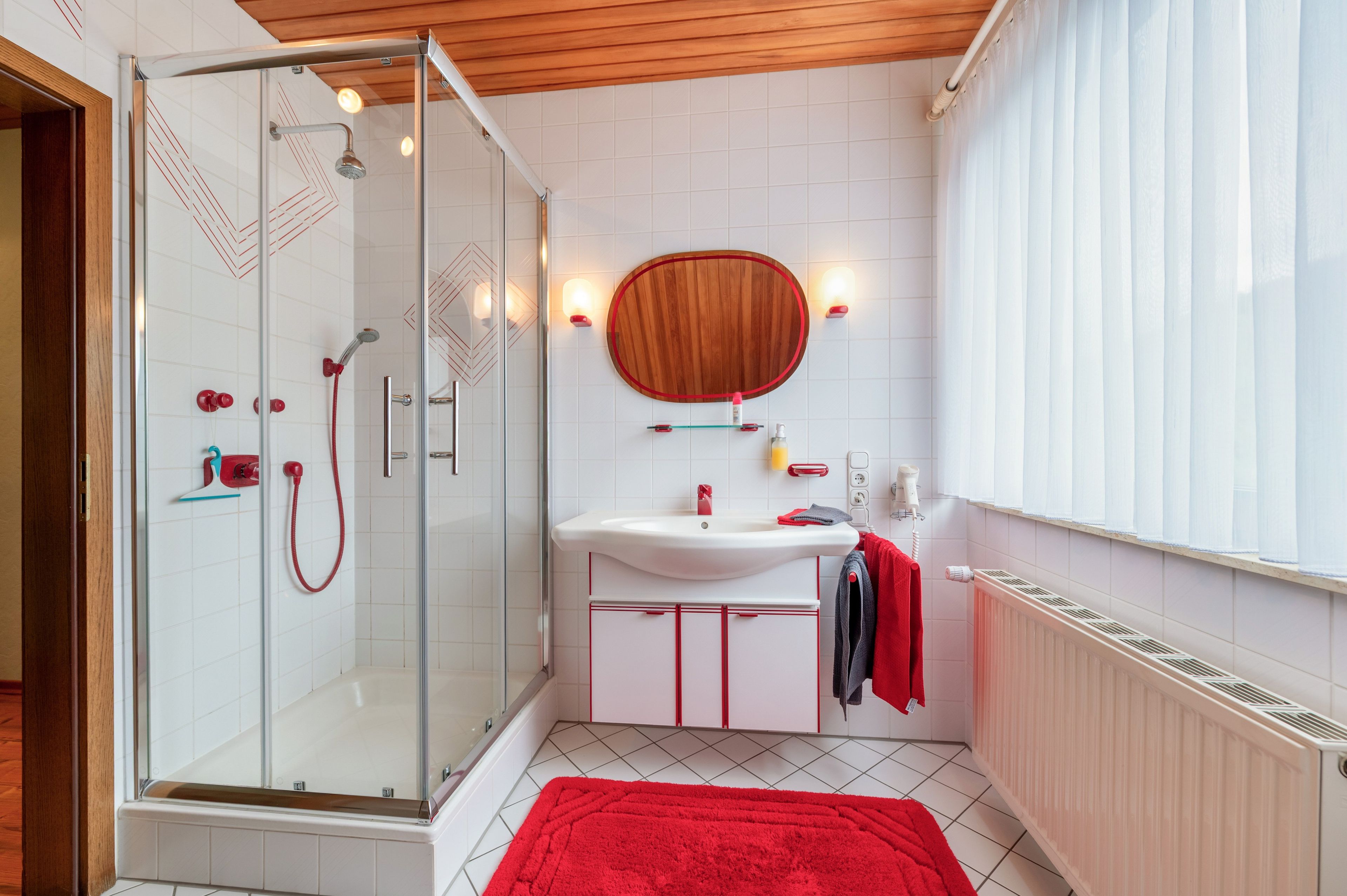 Une salle de bain moderne avec une douche à parois de verre, un meuble-lavabo en bois et une serviette rouge sur le sol.