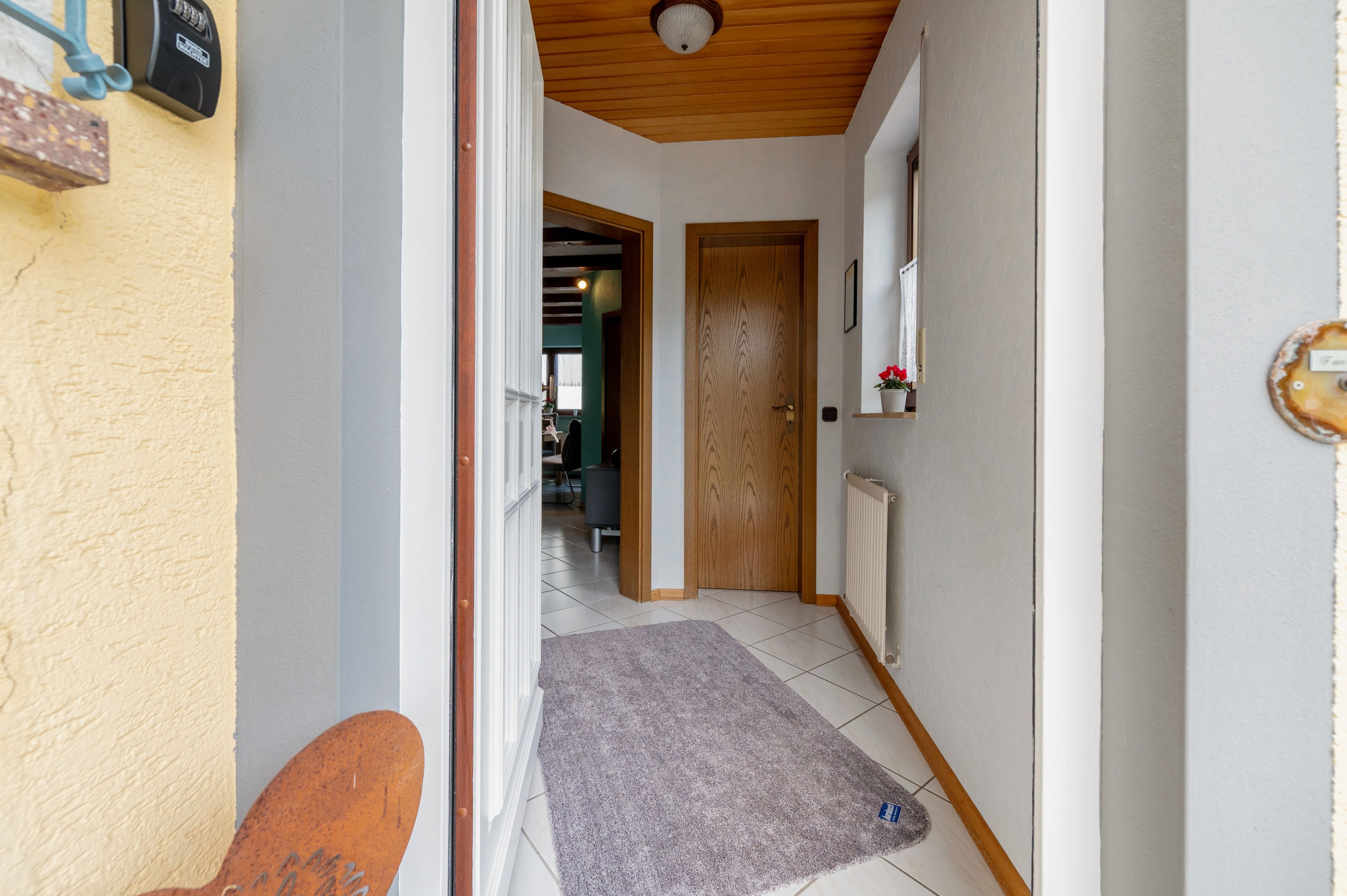 Un couloir avec une porte en bois, un radiateur et un petit tapis sur le sol.