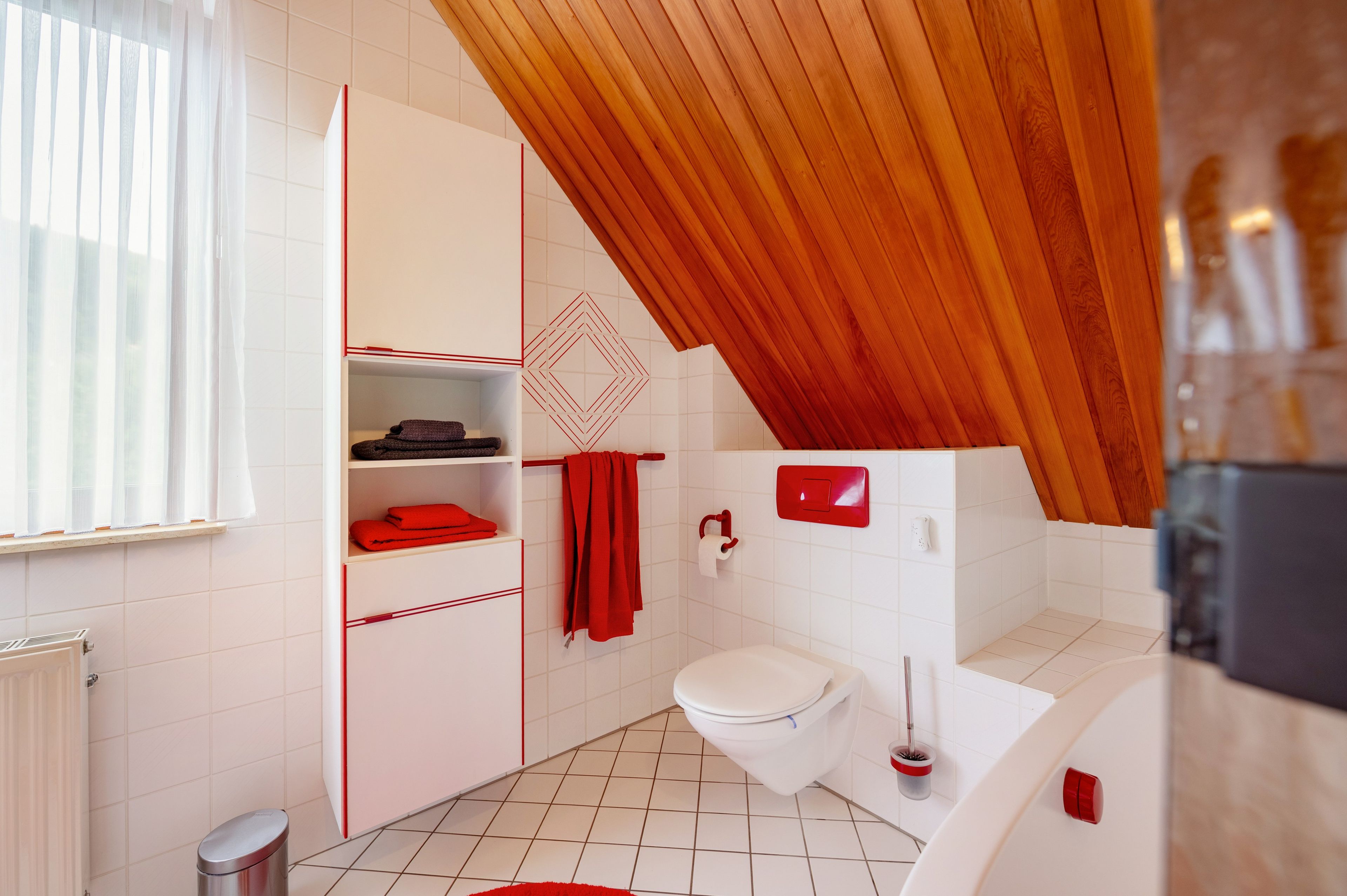 Un bagno moderno con pavimento piastrellato bianco, un water bianco, un porta asciugamani rosso e un asciugamano rosso appeso.