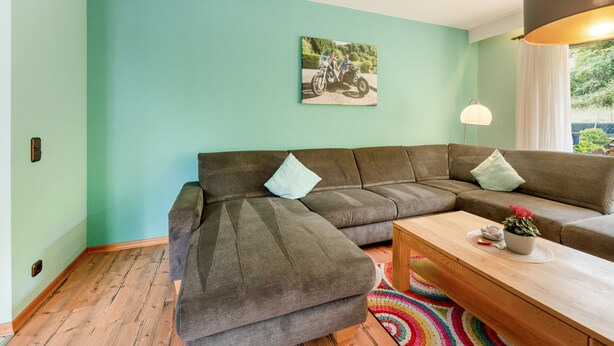 Ein modernes Wohnzimmer mit einem Ecksofa, einem Holztisch und einem farbenfrohen Teppich.