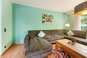 Ein modernes Wohnzimmer mit einem Ecksofa, einem Holztisch und einem farbenfrohen Teppich.