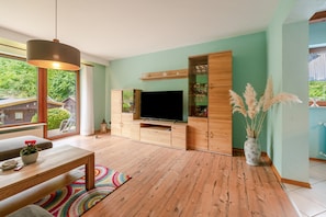 Una sala moderna con un televisor de pantalla plana, armarios de madera, una mesa de comedor y un tapete colorido.