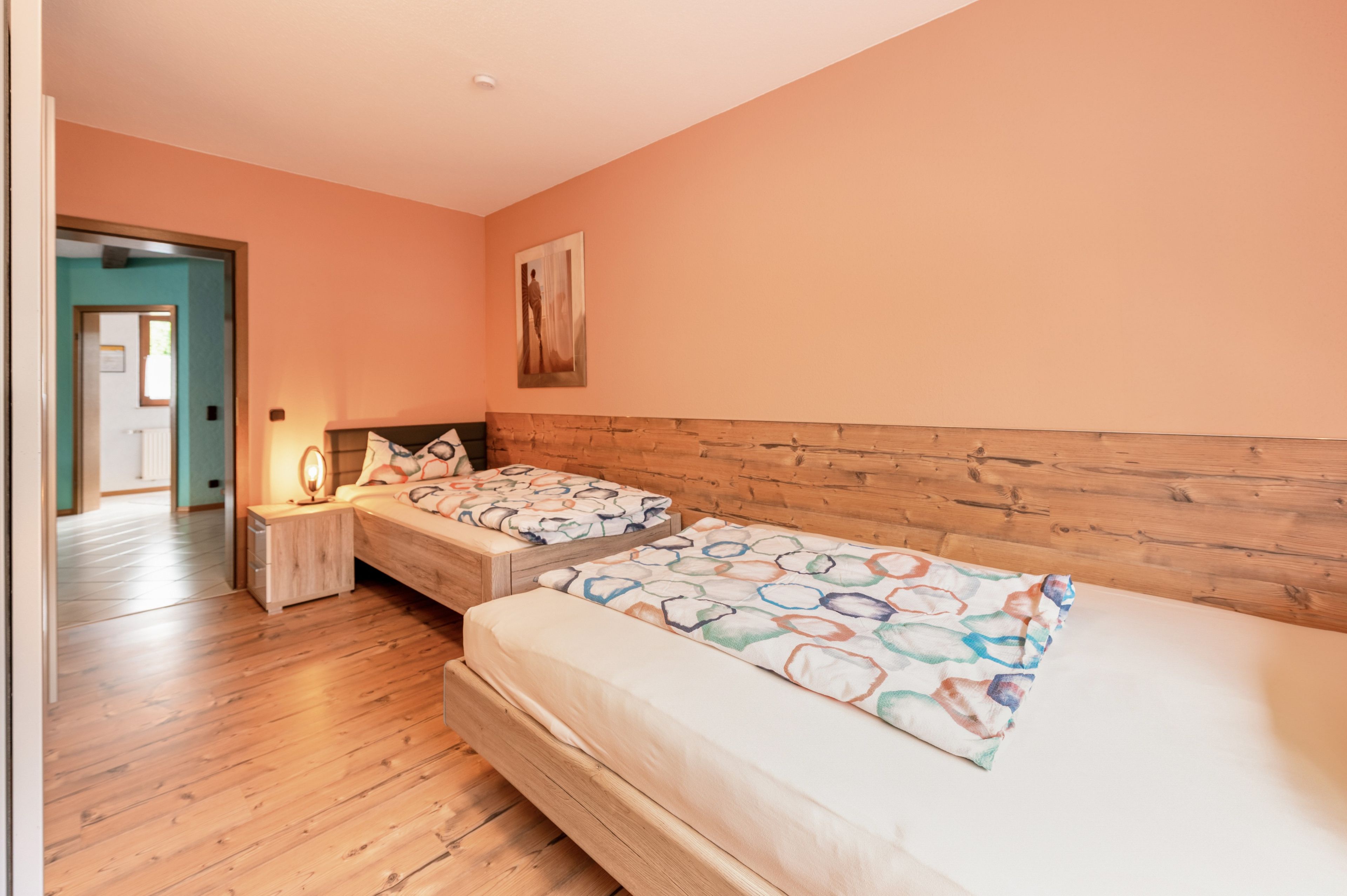 Ein Schlafzimmer mit zwei Betten, einem Holz-Kopfteil, einem Nachttisch mit Lampe und einer Tür zu einem anderen Raum.