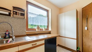 Eine Küche mit Geschirrspüler, einem Fenster mit Spitzenvorhängen und Blick ins Grüne.