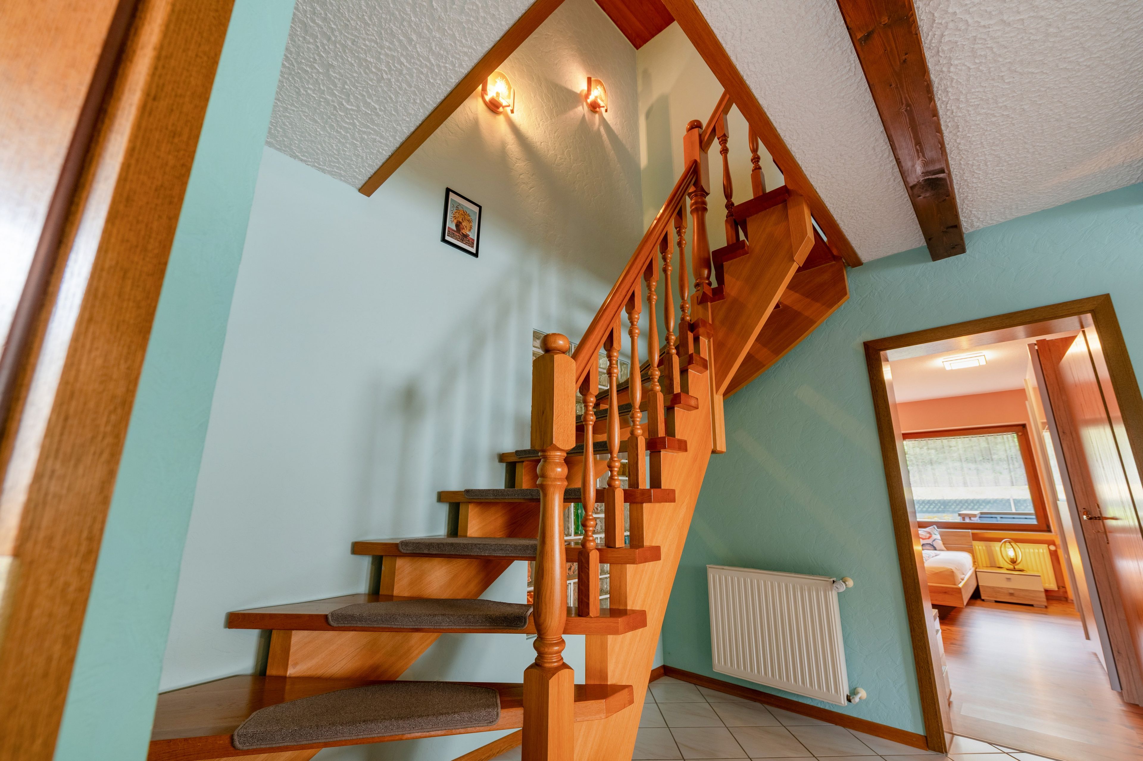 Un escalier en bois avec une rampe, un radiateur et un tableau encadré au mur.