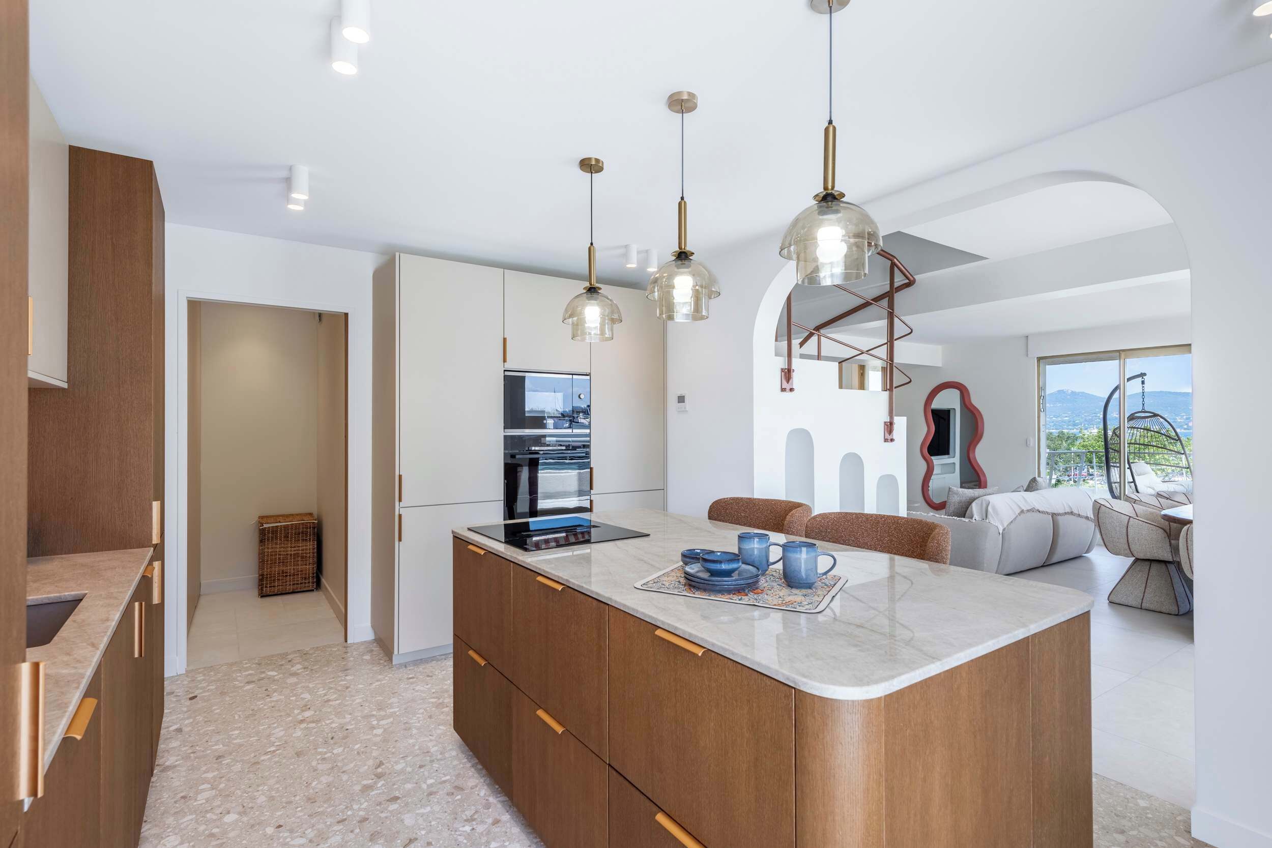Cocina moderna con una isla central, iluminación colgante y vistas al exterior.