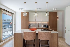 Eine moderne Küche mit Kochinsel, Barhocker, Pendelleuchten und Blick auf einen Balkon.