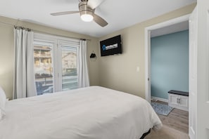 A bedroom with a bed, a ceiling fan, a TV, and a view of the outside through the window.