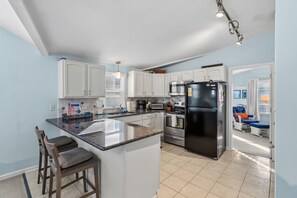 Una cocina moderna con armarios blancos, una isla central con taburetes y un refrigerador negro, además de un microondas.