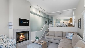 Ett modernt vardagsrum med en öppen spis, en soffgrupp, en tv som är monterad på väggen och en trappa som leder upp till en övre våning.
