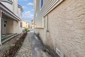 A narrow alleyway between two buildings with a gravel path and a metal fence.