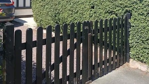A residential property with a gated driveway, a car parked in the driveway, and a well-maintained hedge.