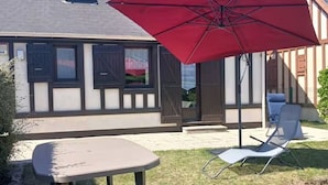 A patio with a table and chairs, a red umbrella, and a building with a sloped roof.