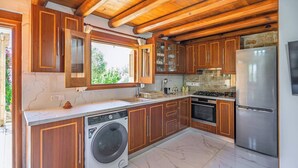 Eine moderne Küche mit Holzausstattung, einer integrierten Waschmaschine, einem Edelstahlkühlschrank und einer Steinwandverkleidung.