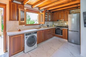 Eine moderne Küche mit Holzausstattung, einer integrierten Waschmaschine, einem Edelstahlkühlschrank und einer Steinwandverkleidung.