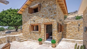 Ein Steinhaus mit Holzdach, einem doppelflügeligen Eingang und einer kleinen Terrasse mit Stufen, die zur Tür hinaufführen.