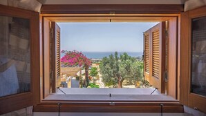 Ein Fenster mit Holzläden, Blick auf das Meer und ein blühender rosa Baum.