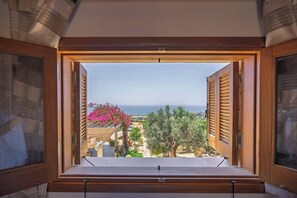 Ein Fenster mit Holzläden, Blick auf das Meer und ein blühender rosa Baum.
