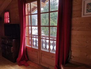 Quarto com uma grande janela, paredes de madeira, um deck de madeira na parte externa e uma televisão à esquerda.