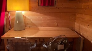A wooden cabin interior with a table, chairs, a lamp, a window with curtains, and a thermostat. - The Red Room (Demi-Quartier)