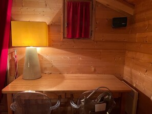 L’intérieur d’un chalet en bois, avec une table, des chaises, une lampe, une fenêtre avec des rideaux et un thermostat.