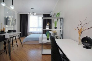 Ein moderner, gut beleuchteter Raum mit Esstisch, Stühlen, einem Bett und einem an der Wand montierten Fernseher.