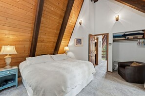 A bedroom with a sloped ceiling, a bed, a nightstand, a lamp, a door leading to a balcony, and a seating area with a chair. - The Rendezvous Chalet – Spacious Mountain Retreat (Breckenridge)