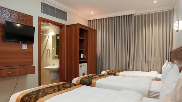 A hotel room with two beds, a TV mounted on the wall, a bathroom with a sink, and a window with curtains. - Palm boutique Makkah Hotel (Makkah)