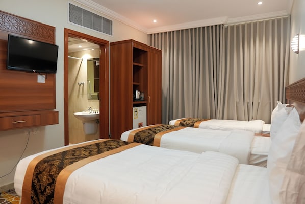 Une chambre d’hôtel avec deux lits, un téléviseur fixé au mur, une salle de bain avec un lavabo et une fenêtre avec des rideaux.