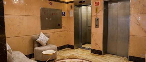 A lobby with a marble floor, a sofa, a small round table, and two elevators.