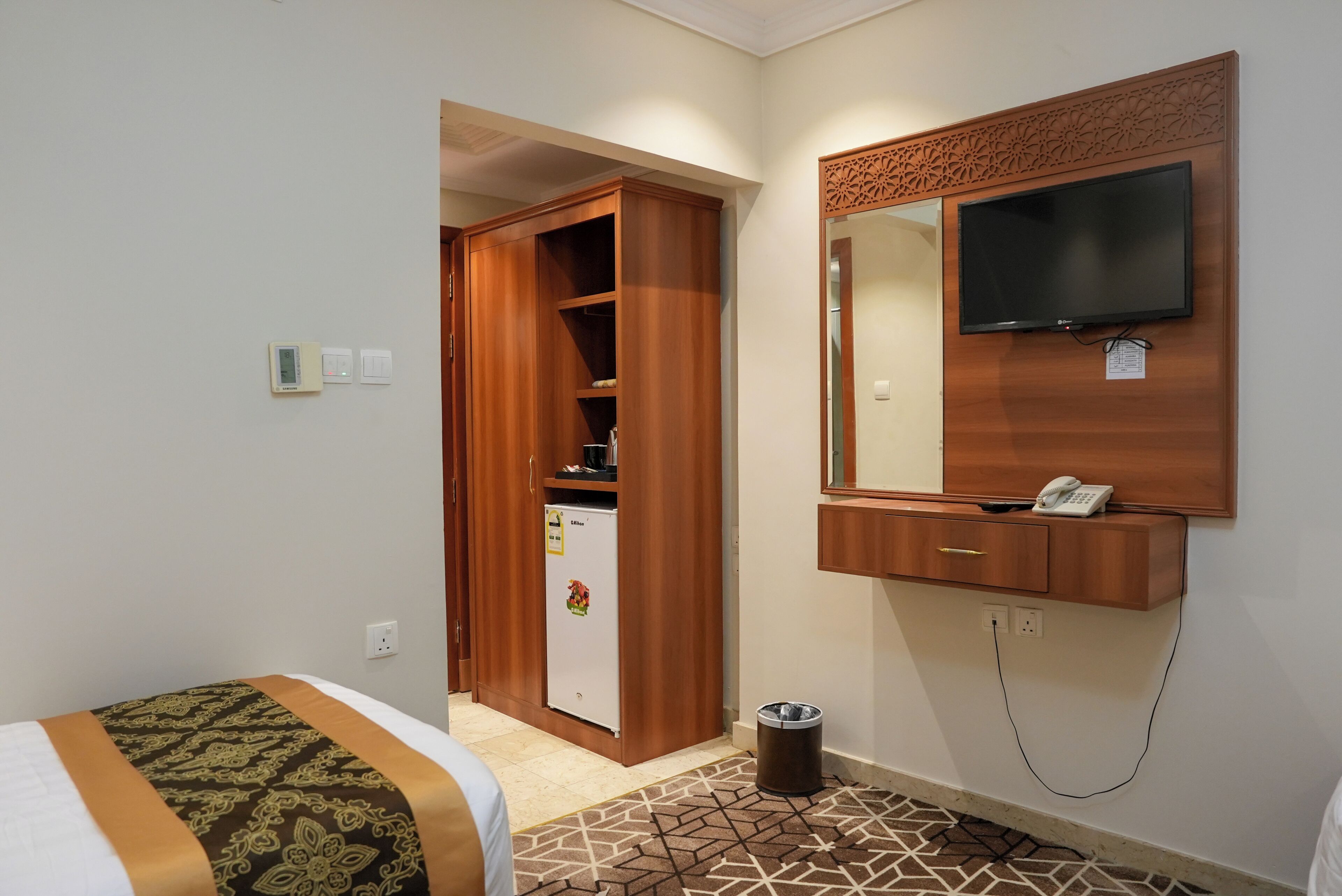 Habitación de hotel con cama, armario, refrigerador, basurero, televisor montado en la pared y teléfono.