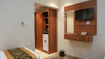 Habitación de hotel con cama, armario, refrigerador, basurero, televisor montado en la pared y teléfono.