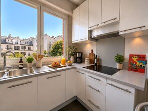 A modern kitchen with white cabinets, a stainless steel sink, and a window overlooking a cityscape. - L'appartement Paul Doumer (Paris)