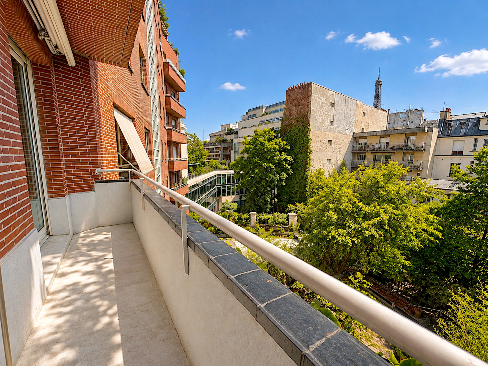 Un balcón con baranda metálica que da a una vista de la ciudad con edificios y árboles.