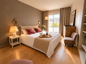 A hotel room with a bed, bedside lamps, a chair, a small table with breakfast, and a view of buildings through the window. - L'appartement Paul Doumer (Paris)