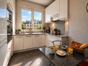 A modern kitchen with a built-in oven, a sink, and a window overlooking a cityscape. - L'appartement Paul Doumer (Paris)