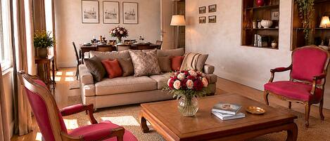 Un salon comprenant un canapé, deux fauteuils, une table basse et un coin repas avec une table dressée pour deux personnes.