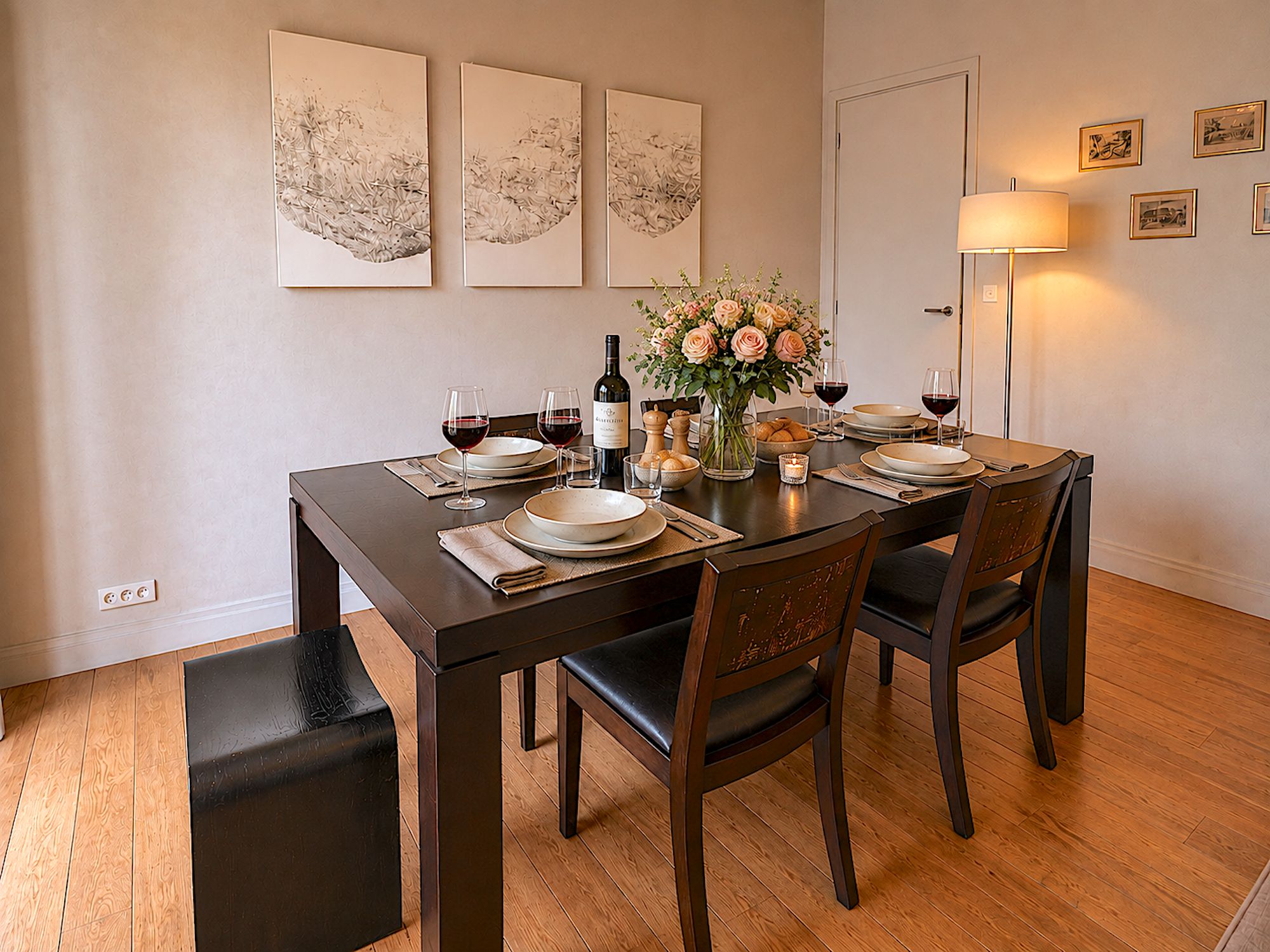 Een eetkamer met een donker houten tafel gedekt voor vier personen, omringd door stoelen. Boven de tafel hangen drie ingelijste kunstwerken aan de muur.