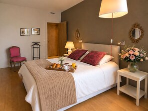 Een verzorgde slaapkamer met een bed, nachtkastje, stoel en een tafeltje met een bloevas.