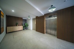 Eine geräumige Lobby mit einer Holzwand, einem Empfangstresen, einer Topfpflanze und einem Aufzug.