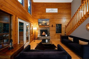 A cozy cabin interior with a fireplace, wooden walls, a sofa, and a sign that reads 'gather'. - Nerf Gun Wall, Theater/Games, Hot Tub, Sleeps 14 (Sevierville)