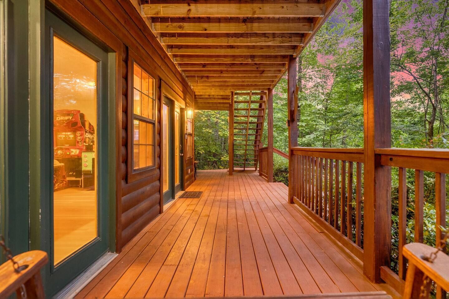 A wooden deck with a railing, leading to a covered porch area with a view of a forested landscape.