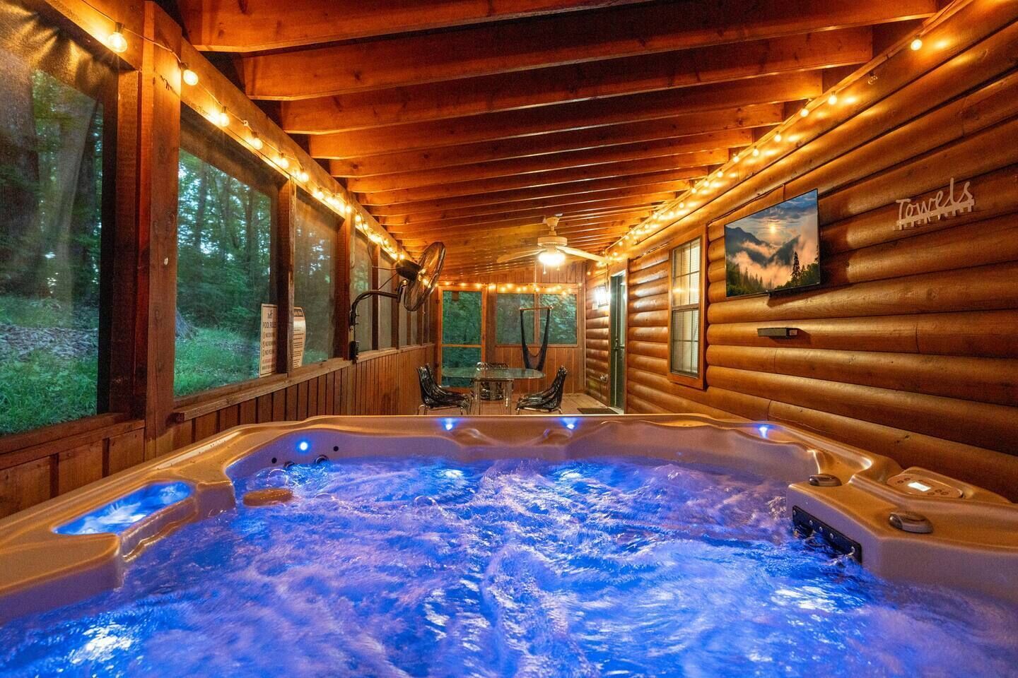 A log cabin interior with a hot tub, wooden walls, and a forest view.