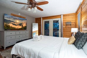 Un dormitorio con cama, ventilador de techo, cómoda, un cuadro y vista por la puerta.