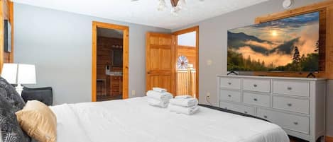 A bedroom with a bed, a ceiling fan, a dresser, a painting, and a door leading to a bathroom.