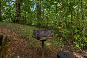 A bench in a forested area with a metal structure attached to it. - Nerf Gun Wall, Theater/Games, Hot Tub, Sleeps 14 (Sevierville)