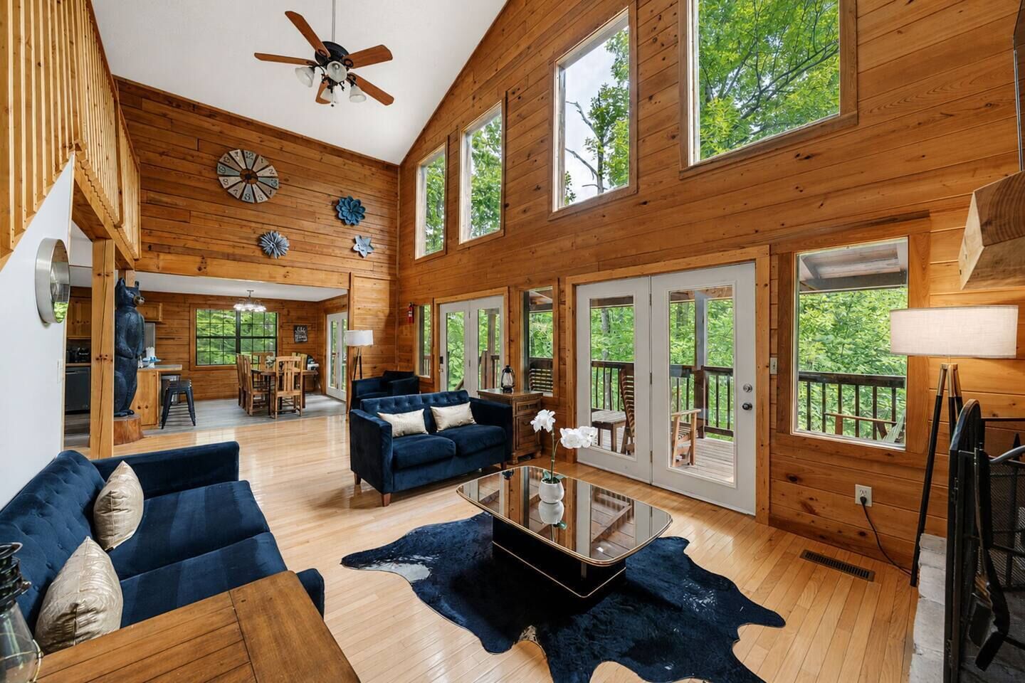 A spacious living room with a blue sofa, wooden floors, and large windows.