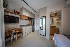 A compact kitchen with a dining area, a refrigerator, and a microwave. There is a small table with two chairs and a TV mounted on the wall. - Nik Sunset  (São Paulo)