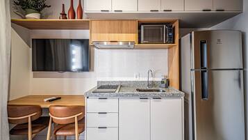 Uma cozinha compacta com micro-ondas embutido, geladeira de aço inoxidável e um pequeno espaço de jantar com mesa e cadeiras.